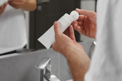 Photo of Man opening tube of cream in bathroom, closeup