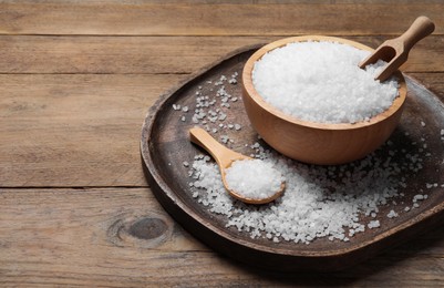 Photo of Bowl, spoon and scoop with natural sea salt on wooden table. Space for text