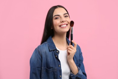 Photo of Beautiful woman applying makeup with brush on pink background