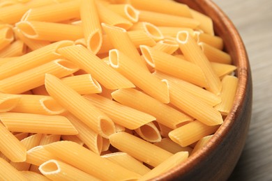 Photo of Raw penne pasta in bowl on table, closeup