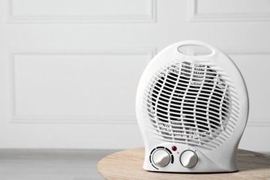 Modern electric fan heater on wooden table indoors, space for text