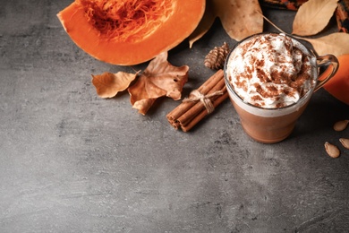 Photo of Delicious pumpkin latte and ingredients on grey table, above view. Space for text