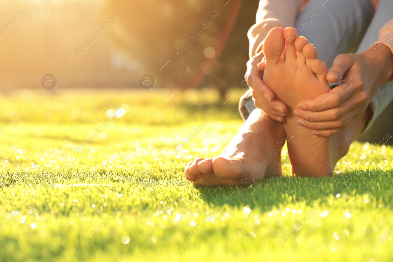 Photo of Young woman sitting barefoot on fresh green grass outdoors, closeup