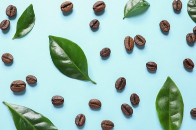 Photo of Fresh green coffee leaves and beans on light blue background, flat lay