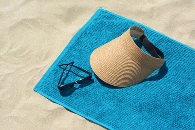 Photo of Towel, straw visor cap and sunglasses on sand. Beach accessories