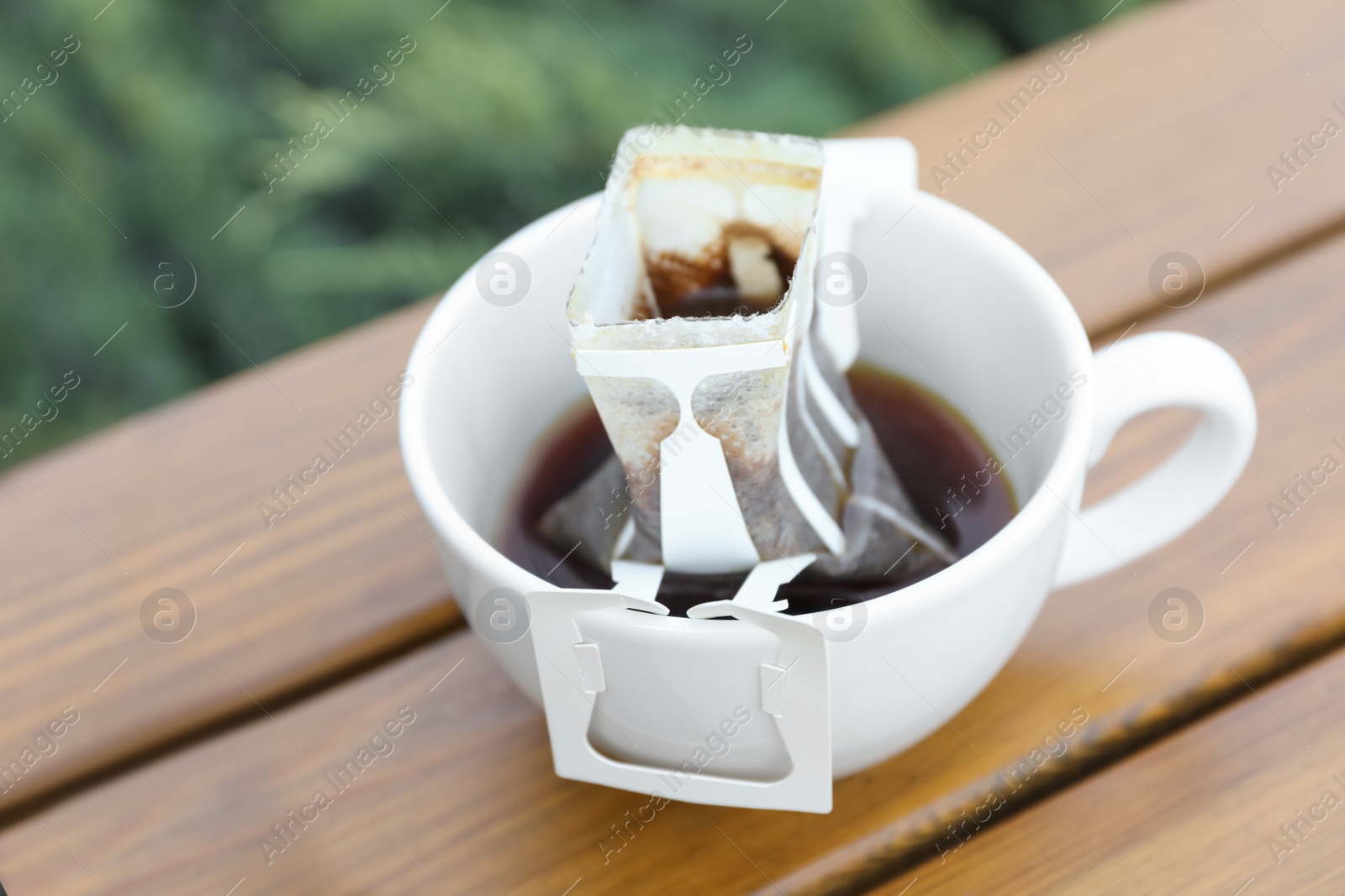 Photo of Cup with drip coffee bag on wooden table, closeup