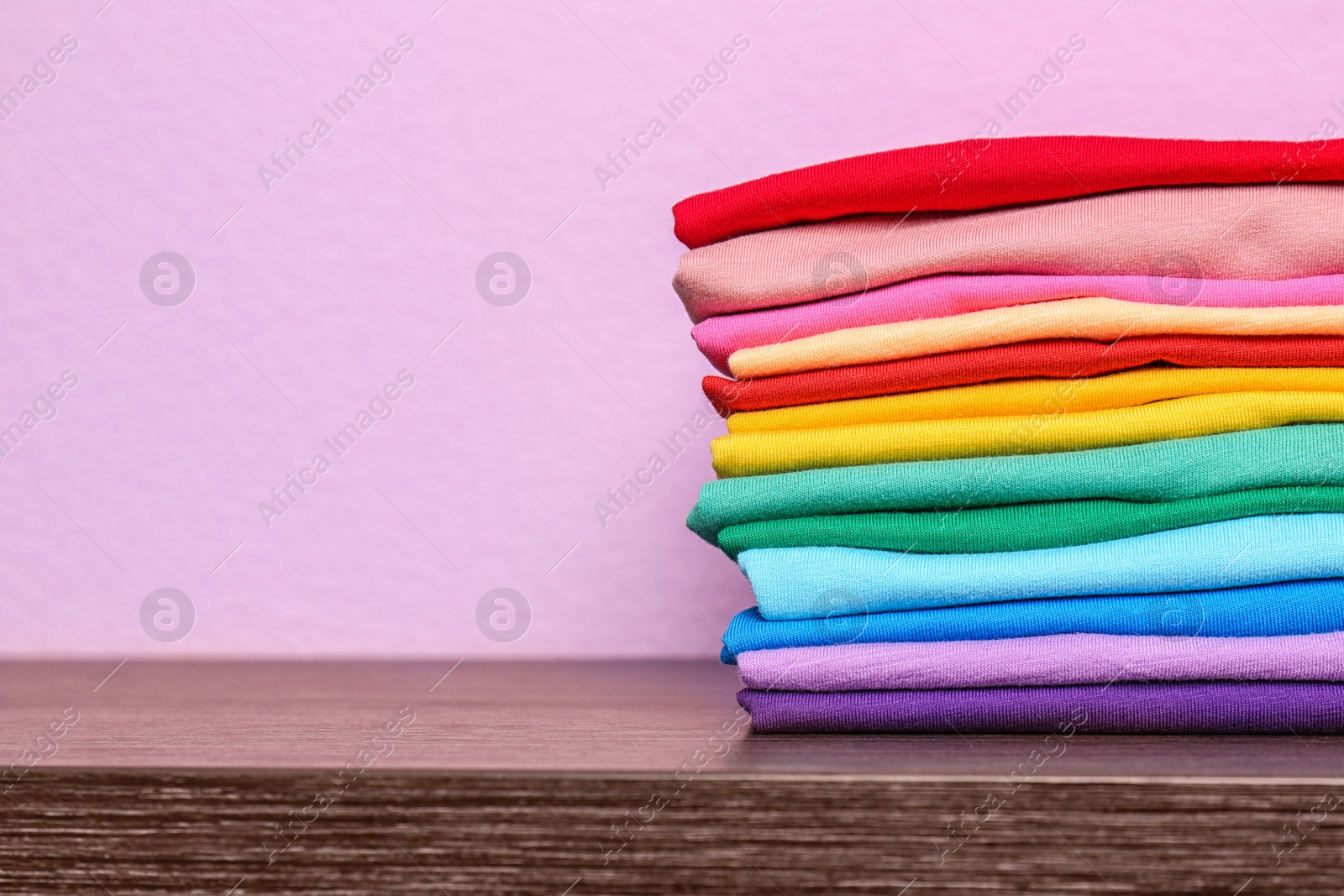 Photo of Stack of colorful t-shirts on table against color background