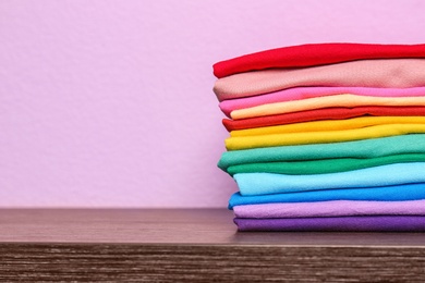 Photo of Stack of colorful t-shirts on table against color background