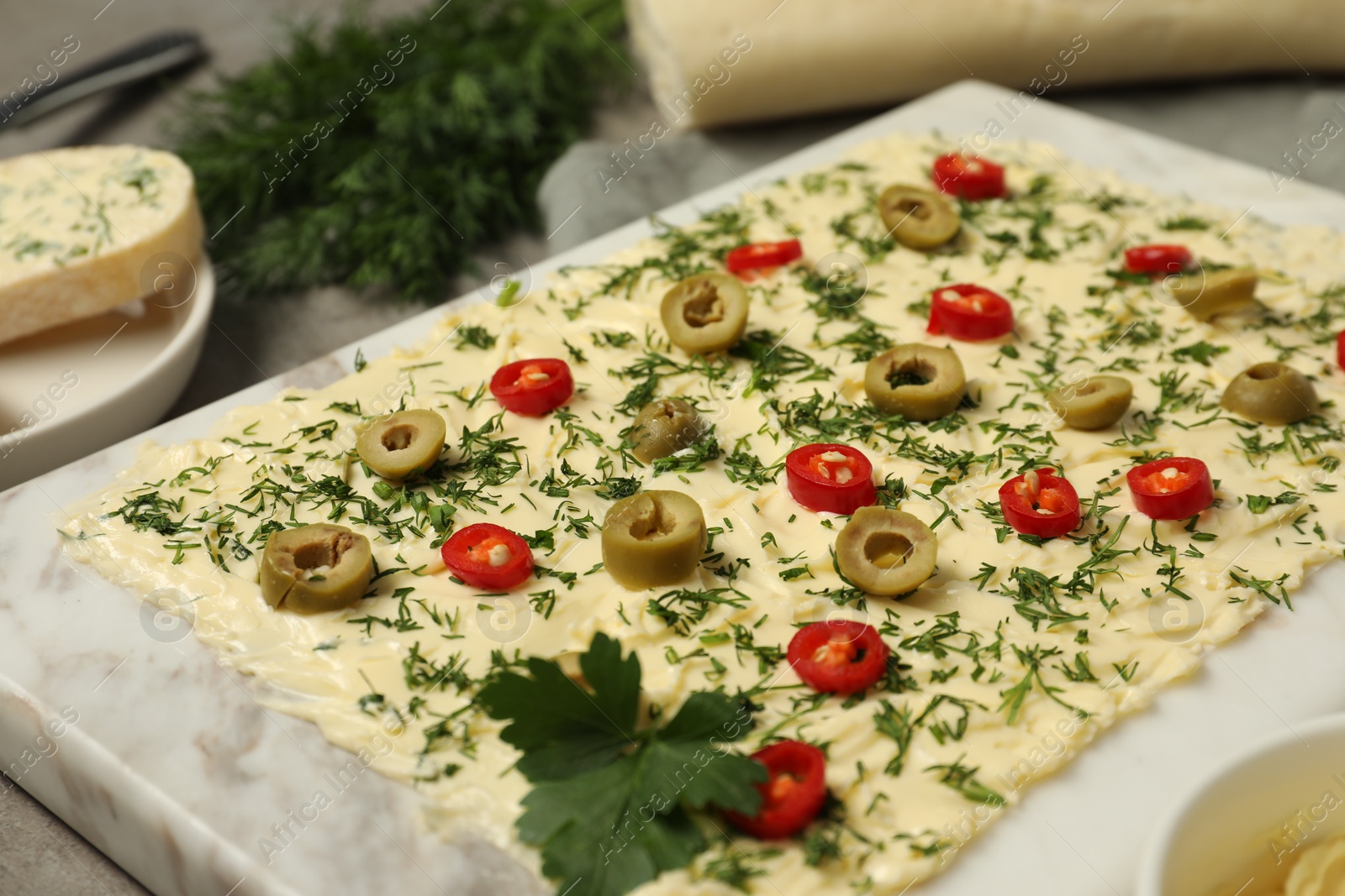 Photo of Fresh butter board with cut olives, dill and pepper on grey table, closeup