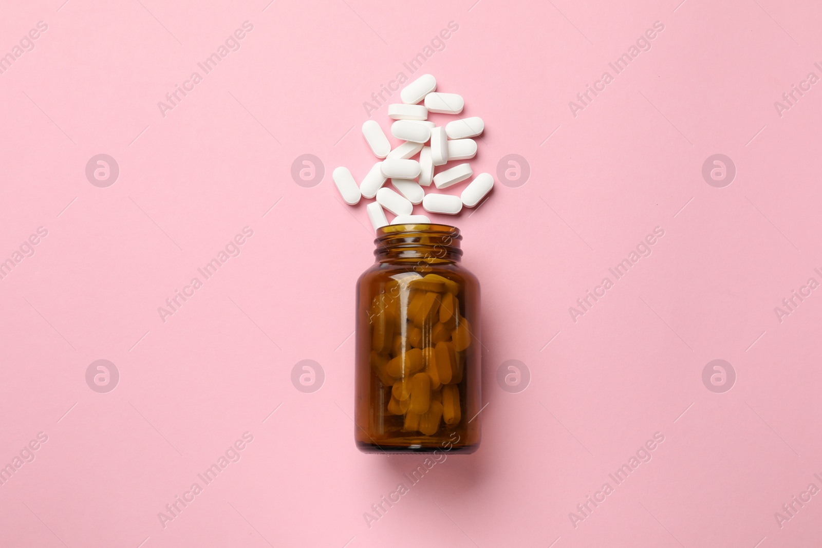 Photo of Bottle and vitamin capsules on pink background, top view