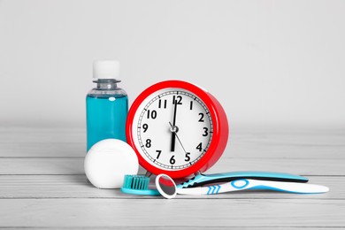 Composition with dental floss, alarm clock and different teeth care products on white wooden table