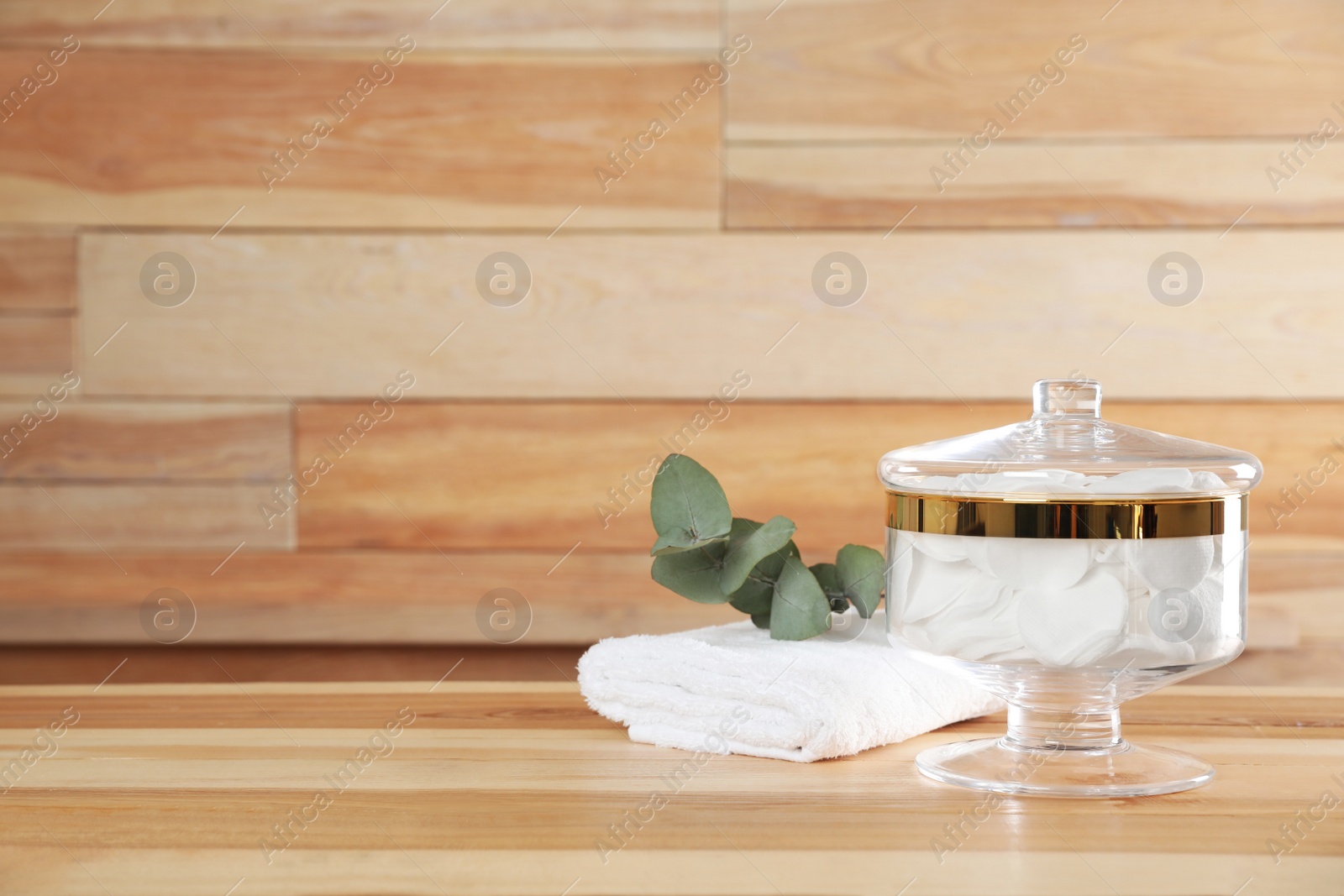 Photo of Decorative glass jar with cotton pads and towel on table against wooden background. Space for text