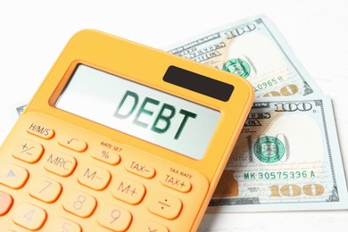 Calculator with word Debt and money on white table, closeup