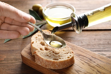 Photo of Man pouring fresh olive oil into spoon over bread at table, closeup