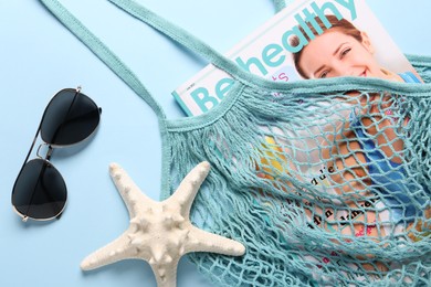 String bag, sunglasses, starfish and magazine on light blue background, top view