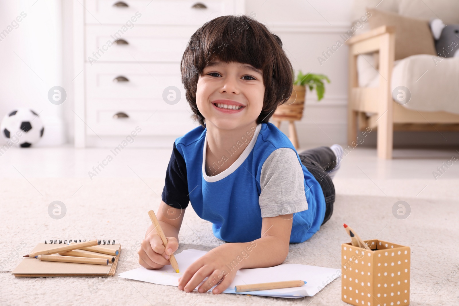 Photo of Cute little boy drawing with pencils on floor at home