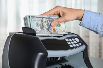 Photo of Woman putting money into counting machine indoors, closeup