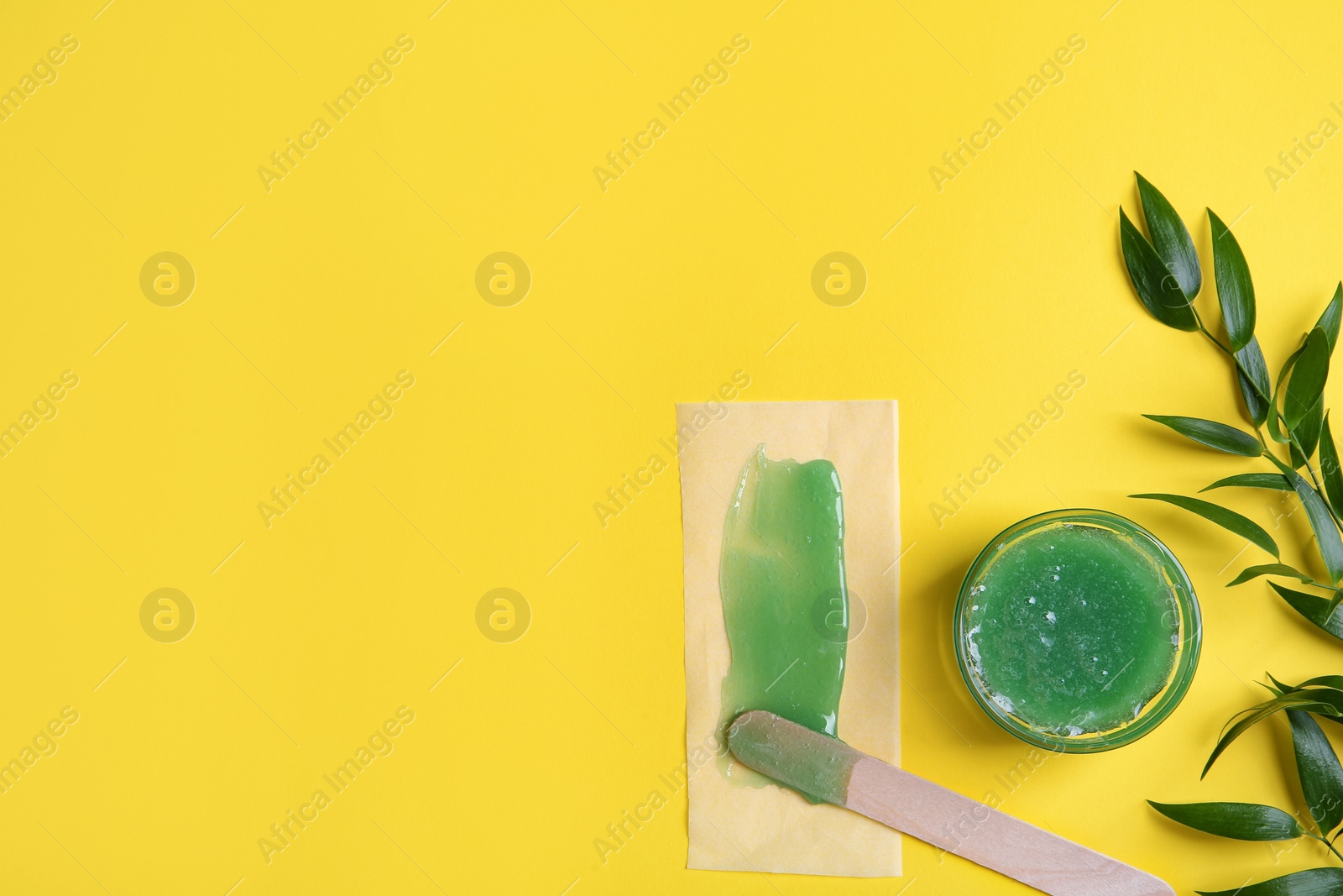 Photo of Spatula with wax, paper and leaves on yellow background, flat lay. Space for text