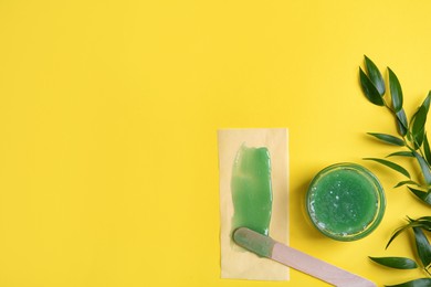 Spatula with wax, paper and leaves on yellow background, flat lay. Space for text