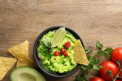 Delicious guacamole with nachos chips and ingredients on wooden table, flat lay. Space for text