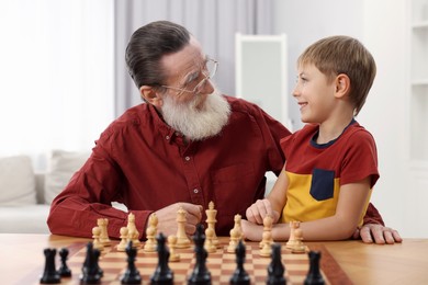 Senior man teaching his grandson to play chess at home