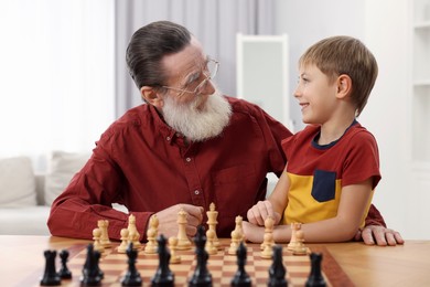 Photo of Senior man teaching his grandson to play chess at home