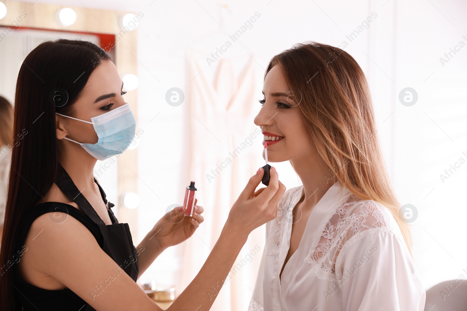 Photo of Makeup artist in protective mask working with woman indoors. Preventive measures during COVID-19 pandemic