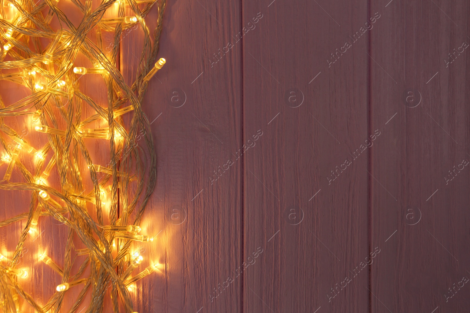 Photo of Glowing Christmas lights on pink wooden background, top view. Space for text