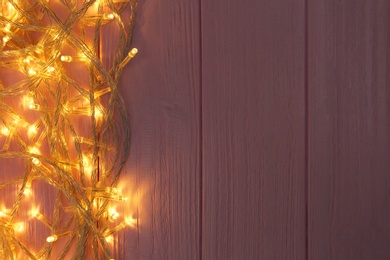 Glowing Christmas lights on pink wooden background, top view. Space for text