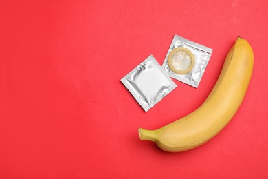 Photo of Condoms with banana and space for text on red background, flat lay. Safe sex