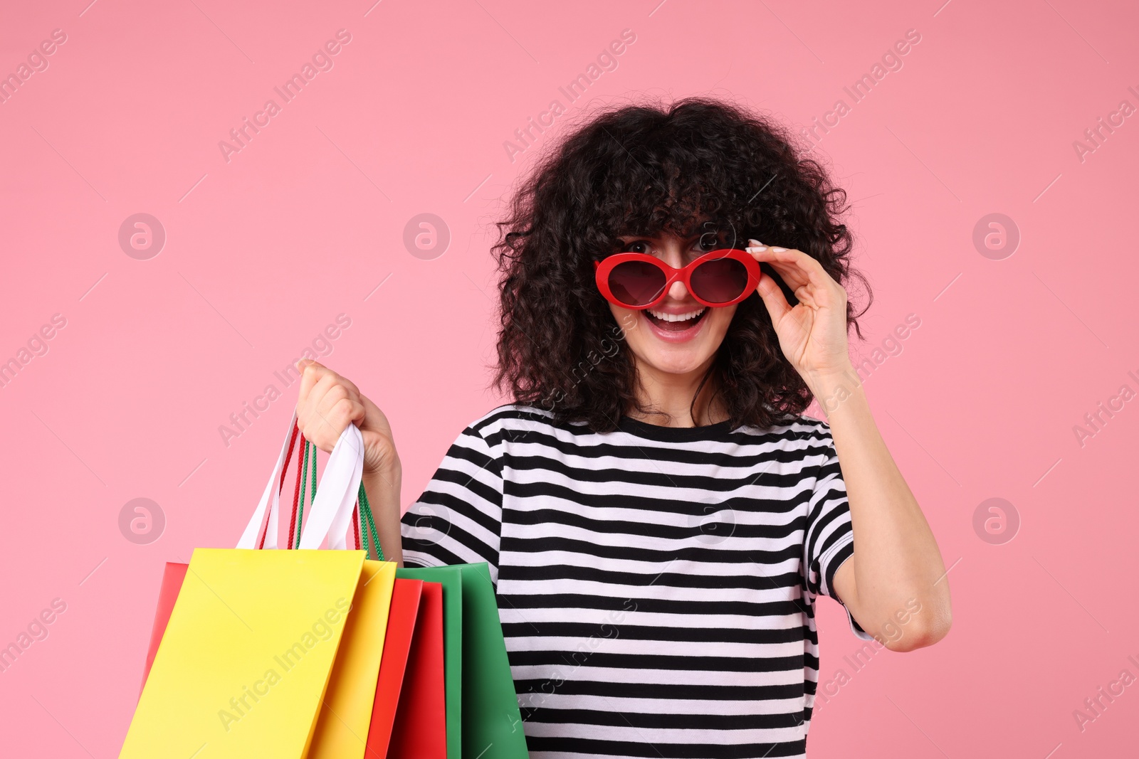 Photo of Happy young woman with shopping bags and stylish sunglasses on pink background