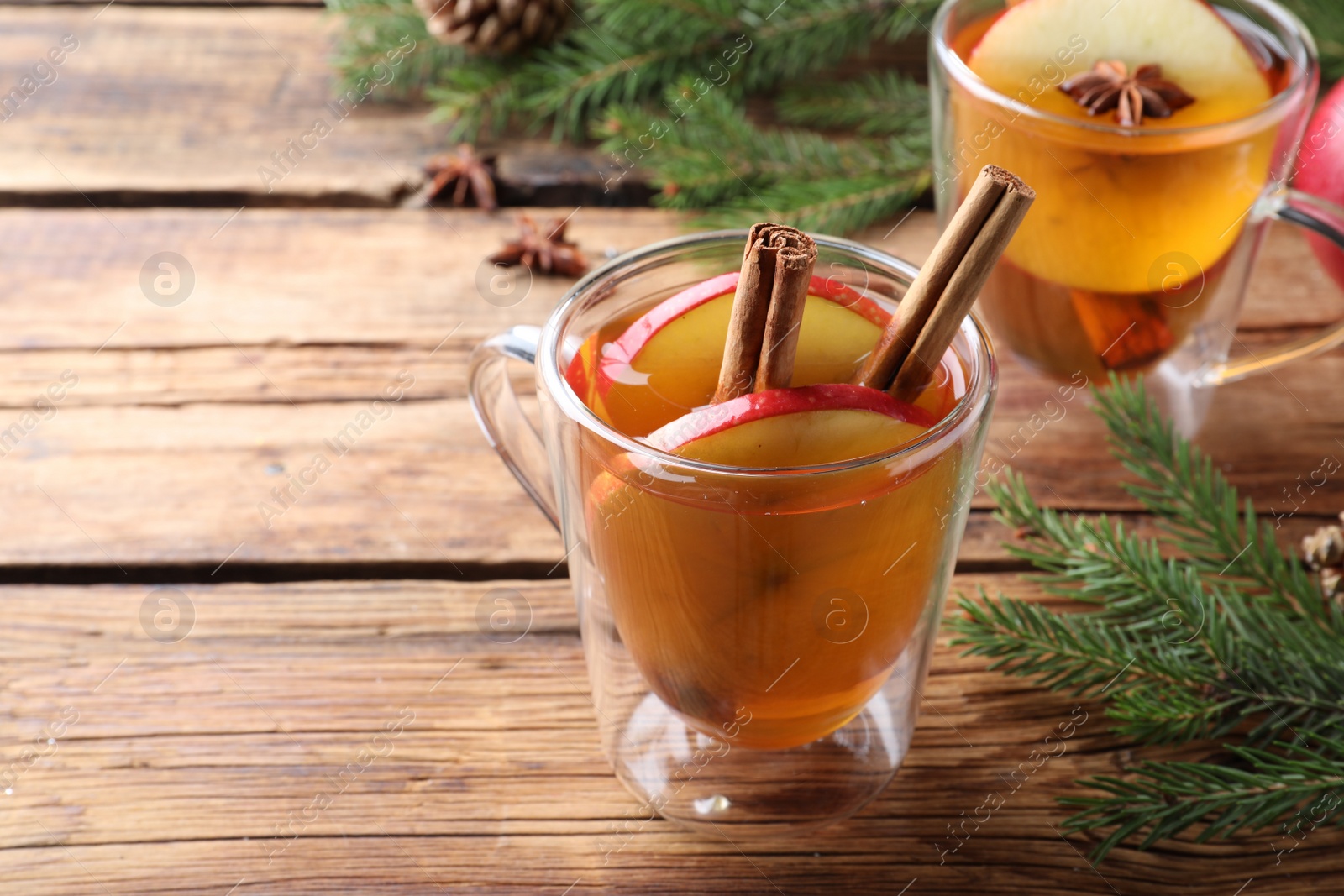 Photo of Hot mulled cider and fir branches on wooden table, space for text