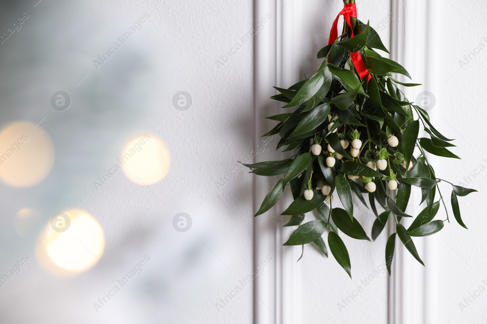 Photo of Mistletoe bunch with red ribbon hanging on light background, space for text. Bokeh effect