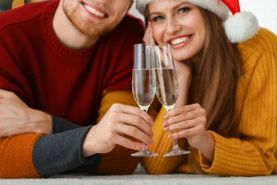 Happy young couple with glasses of champagne at home, focus on hands. Christmas celebration