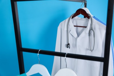 Photo of Medical uniforms on metal rack against light blue background