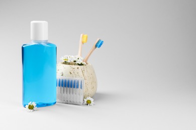 Composition with fresh mouthwash in bottle, toothbrushes and interdental brushes on grey background. Space for text