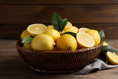 Photo of Many fresh ripe lemons with green leaves on wooden table