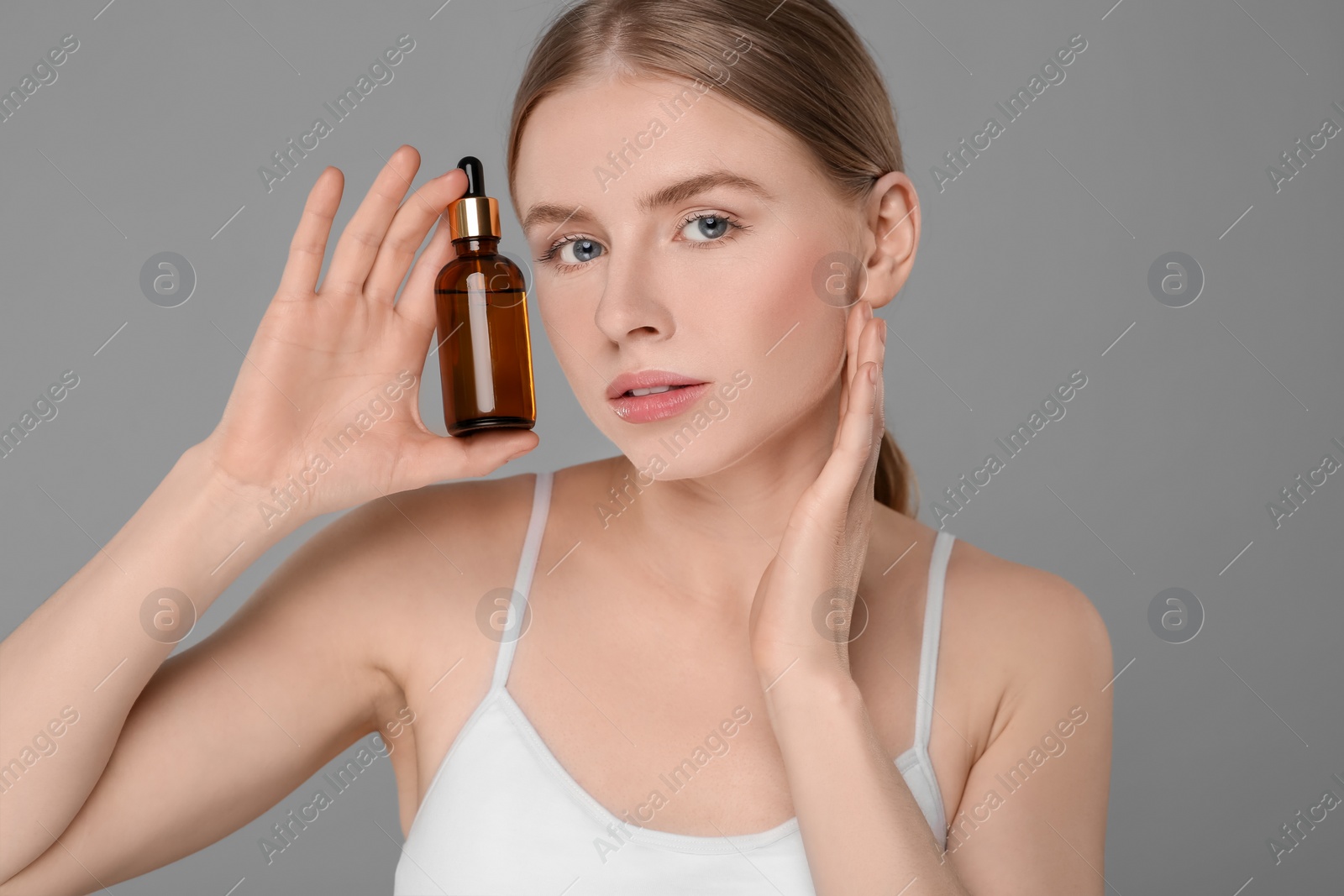 Photo of Beautiful young woman with bottle of essential oil on light grey background