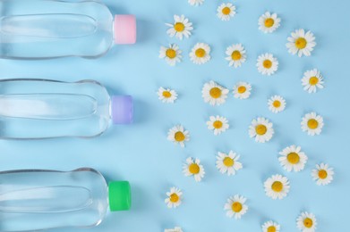 Bottles with baby oil and daisies on light blue background, flat lay