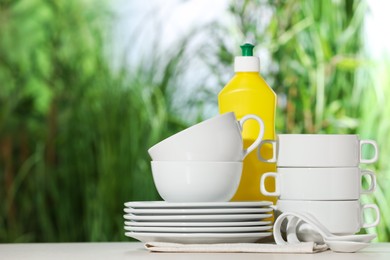 Set of clean dishware and detergent on white table against blurred background, space for text