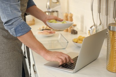 Man making dinner while watching online cooking course via laptop in kitchen, closeup