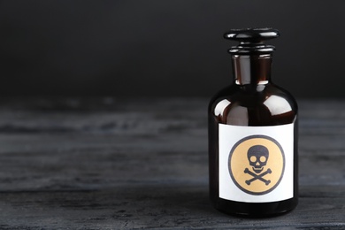 Photo of Glass bottle of poison with warning sign on black wooden table. Space for text