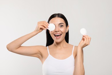 Photo of Young woman using cotton pads with micellar water on light grey background