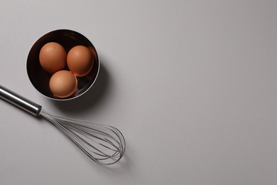Photo of Metal whisk and raw eggs on grey background, flat lay. Space for text