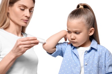 Mother applying ointment onto her daughter's elbow against white background