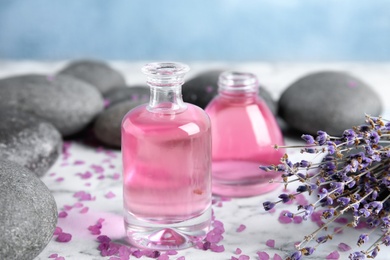 Photo of Natural herbal oil and lavender flowers on table against blurred background