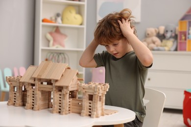 Photo of Little boy playing with wooden entry gate at white table in room. Child's toy