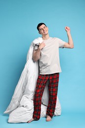 Happy man in pyjama holding blanket on light blue background