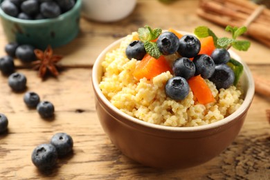 Photo of Tasty millet porridge with blueberries, pumpkin and mint in bowl on wooden table, closeup