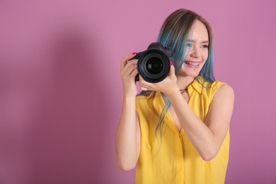 Young female photographer with camera on color background